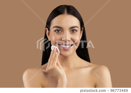 Pretty brunette woman touching her face with cotton pad, closeup 96773489