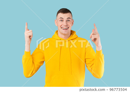 Look up. Happy caucasian guy pointing fingers upward, showing something over blue background, studio shot Look up. Happy caucasian guy pointing fingers upward, showing something over blue background, studio shot 96773504
