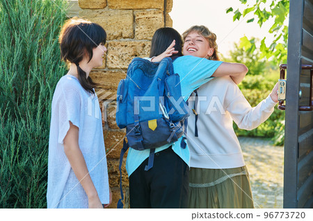 Meeting of friends, young female with guy and girl joyfully hugging near front door Meeting of friends, young female with guy and girl joyfully hugging near front door 96773720