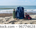 A thermos of tea and a backpack against the backdrop of nature. Walking along the seashore. 96774628