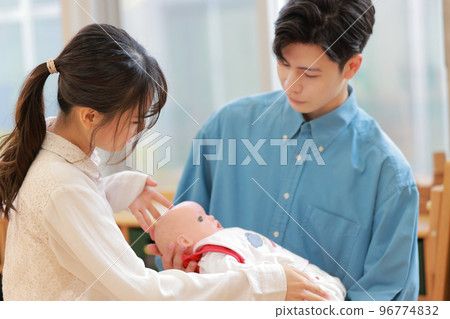 A man learning how to hold a baby and an instructor teaching him_1 A man learning how to hold a baby and an instructor teaching him_1 96774832