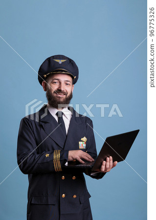 Smiling airliner pilot using laptop, typing message side view. Middle aged aviator in professional flight uniform holding portable computer in airport, browsing internet, online connection Smiling airliner pilot using laptop, typing message side view. Middle aged aviator in professional flight uniform holding portable computer in airport, browsing internet, online connection 96775326