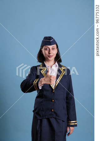 Smiling flight attendant showing thumbs up gesture, aviation academy stewardess doing approval sign. Young attractive air hostess in professional uniform approving, studio shot Smiling flight attendant showing thumbs up gesture, aviation academy stewardess doing approval sign. Young attractive air hostess in professional uniform approving, studio shot 96775332