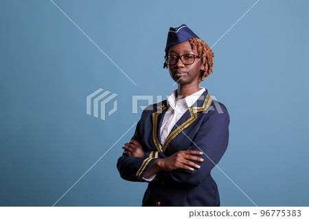Serious female african american airline attendant analyzing options for upcoming flight itineraries at work. Stewardess wearing uniform in studio shot against blue background. Serious female african american airline attendant analyzing options for upcoming flight itineraries at work. Stewardess wearing uniform in studio shot against blue background. 96775383
