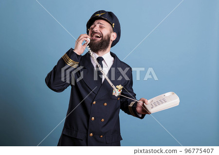 Middle aged airliner captain talking on landline phone, holding telephone, having conversation. Smiling pilot in professional flight uniform answering call in airport, studio medium shot Middle aged airliner captain talking on landline phone, holding telephone, having conversation. Smiling pilot in professional flight uniform answering call in airport, studio medium shot 96775407