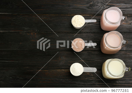 Protein shakes and powder on black wooden table, flat lay. Space for text 96777281