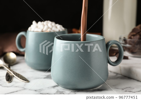 Pouring hot cocoa drink into cup on white marble table 96777451