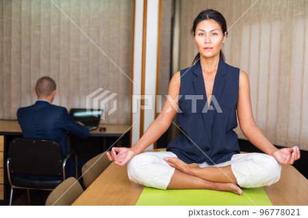 Businesswoman sitting at the table in lotus position 96778021