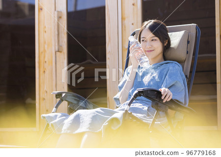 Sauna girls wearing a sauna poncho and taking an open air bath in front of an outdoor sauna 96779168