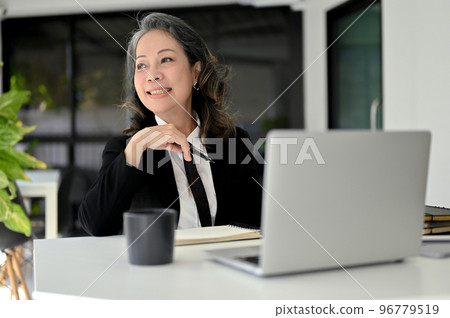 Cheerful Asian aged businesswoman daydreaming, smiling and looking out the window. Cheerful Asian aged businesswoman daydreaming, smiling and looking out the window. 96779519