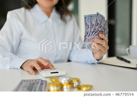 cropped image, An Asian aged woman using calculator, holding US dollar banknotes cropped image, An Asian aged woman using calculator, holding US dollar banknotes 96779554