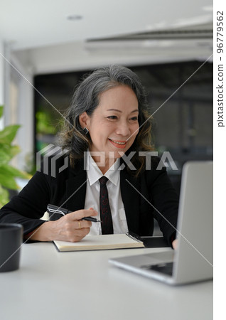 Charming Asian aged businesswoman working at her desk, using laptop computer. Charming Asian aged businesswoman working at her desk, using laptop computer. 96779562