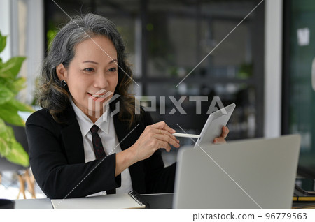 Beautiful Asian aged businesswoman working at her desk, using laptop and tablet Beautiful Asian aged businesswoman working at her desk, using laptop and tablet 96779563