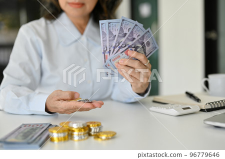 A successful and wealth Asian aged female holding US dollar bills and coins. cropped image 96779646