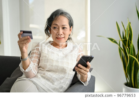 Beautiful Asian retire woman using her smartphone and credit card to pay an online bills Beautiful Asian retire woman using her smartphone and credit card to pay an online bills 96779653