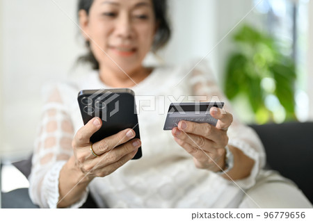 close-up, An attractive Asian retire woman using her smartphone and holding a credit card 96779656