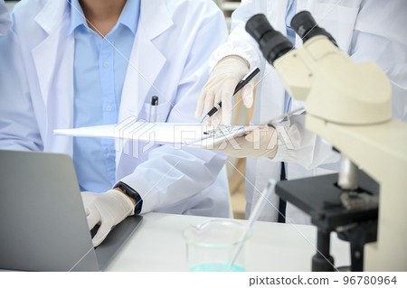 cropped, A professional scientist working in the lab with his coworker, using laptop and microscope. cropped, A professional scientist working in the lab with his coworker, using laptop and microscope. 96780964