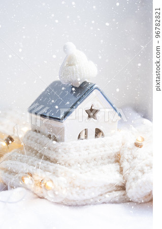 Cozy house is wrapped in a hat and scarf in a snowstorm -window sill decor. Winter, snow - home insulation, protection from cold and bad weather, room heating system. Festive mood, Christmas, New Year Cozy house is wrapped in a hat and scarf in a snowstorm -window sill decor. Winter, snow - home insulation, protection from cold and bad weather, room heating system. Festive mood, Christmas, New Year 96782821