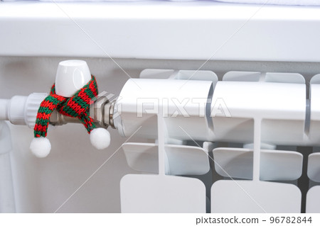 Radiator in the house is wrapped in a knitted scarf and a hat. Warmth and comfort in the house, insulation, winterization. Festive decor for Christmas and New Year. Saving heat, gas in a crisis 96782844