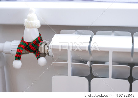 Radiator in the house is wrapped in a knitted scarf and a hat. Warmth and comfort in the house, insulation, winterization. Festive decor for Christmas and New Year. Saving heat, gas in a crisis 96782845
