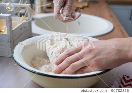 Hands knead thick dough on the kitchen table, decorated with festive decorations for Christmas and New year. Baking at home, aroma and comfort. Close-up 96782856