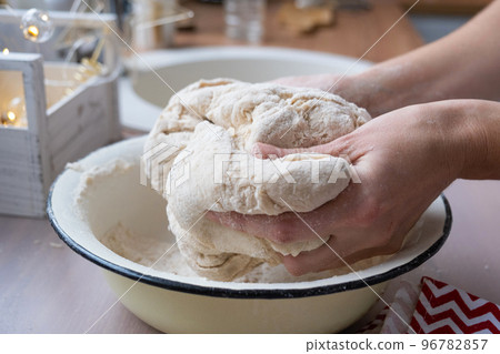 Hands knead thick dough on the kitchen table, decorated with festive decorations for Christmas and New year. Baking at home, aroma and comfort. Close-up 96782857