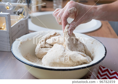 Hands knead thick dough on the kitchen table, decorated with festive decorations for Christmas and New year. Baking at home, aroma and comfort. Close-up Hands knead thick dough on the kitchen table, decorated with festive decorations for Christmas and New year. Baking at home, aroma and comfort. Close-up 96782859