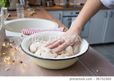 Hands knead thick dough on the kitchen table, decorated with festive decorations for Christmas and New year. Baking at home, aroma and comfort. Close-up Hands knead thick dough on the kitchen table, decorated with festive decorations for Christmas and New year. Baking at home, aroma and comfort. Close-up 96782860
