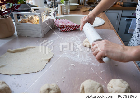 Hands knead thick dough, roll out with a rolling pin on the kitchen table, decorated with festive decorations for Christmas and New year. Baking at home, aroma and comfort. 96782869