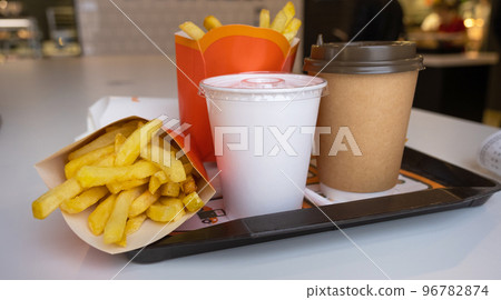 Fast food on a tray in a restaurant. French fries, a glass with a milkshake, coffee 96782874