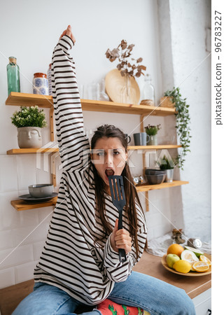 Funny woman singing into spatula, holding spatula as microphone. 96783227
