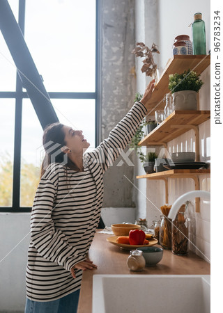Woman takes out a glass from shelf in the kitchen 96783234