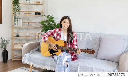 Asian female artist playing the guitar and singing happily in the living room, Relaxation with music therapy, Spending free time with music, Joy of playing music, Acoustic guitar. Asian female artist playing the guitar and singing happily in the living room, Relaxation with music therapy, Spending free time with music, Joy of playing music, Acoustic guitar. 96783273