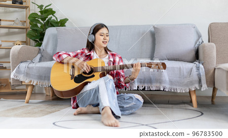 Asian female artist playing the guitar and singing happily in the living room, Relaxation with music therapy, Spending free time with music, Joy of playing music, Acoustic guitar. 96783500