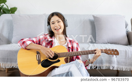 Asian female artist playing the guitar and singing happily in the living room, Relaxation with music therapy, Spending free time with music, Joy of playing music, Acoustic guitar. 96783970