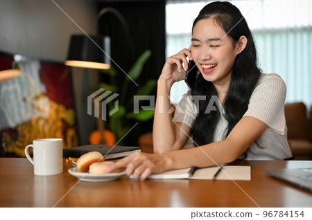 Cheerful Asian female college student enjoys talking on the phone with someone Cheerful Asian female college student enjoys talking on the phone with someone 96784154