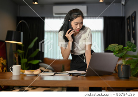 Asian businesswoman talking on the phone with client while looking the details on laptop screen. Asian businesswoman talking on the phone with client while looking the details on laptop screen. 96784159
