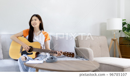 Asian female artist playing the guitar and singing happily in the living room, Relaxation with music therapy, Spending free time with music, Joy of playing music, Acoustic guitar. Asian female artist playing the guitar and singing happily in the living room, Relaxation with music therapy, Spending free time with music, Joy of playing music, Acoustic guitar. 96785107