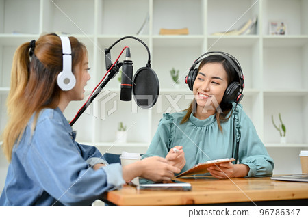 Happy Asian female radio guest enjoys talking with a professional female radio host Happy Asian female radio guest enjoys talking with a professional female radio host 96786347