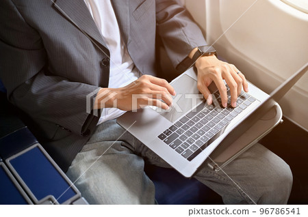 A professional businessman in formal suit is using notebook laptop during the flight. cropped image 96786541