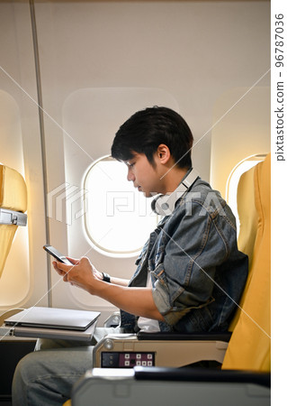 Hipster Asian male traveler or passenger in an economy seat, using his smartphone 96787036