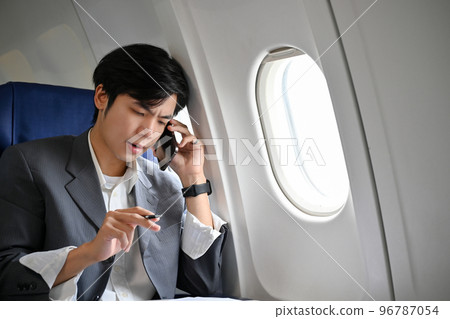 Stressed and professional Asian businessman having a serious phone call during the flight Stressed and professional Asian businessman having a serious phone call during the flight 96787054