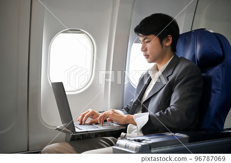 Professional Asian businessman working on portable laptop during the flight for his business trip Professional Asian businessman working on portable laptop during the flight for his business trip 96787069