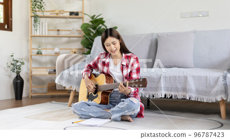 Asian female artist playing the guitar and singing happily in the living room, Relaxation with music therapy, Spending free time with music, Joy of playing music, Acoustic guitar. Asian female artist playing the guitar and singing happily in the living room, Relaxation with music therapy, Spending free time with music, Joy of playing music, Acoustic guitar. 96787423