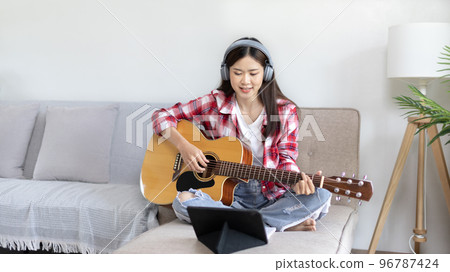 Asian female artist playing the guitar and singing happily in the living room, Relaxation with music therapy, Spending free time with music, Joy of playing music, Acoustic guitar. Asian female artist playing the guitar and singing happily in the living room, Relaxation with music therapy, Spending free time with music, Joy of playing music, Acoustic guitar. 96787424