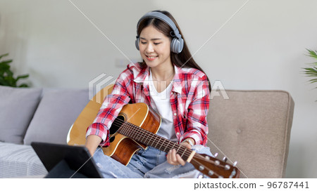 Woman practicing or learning to play guitar and practice using his fingers to hold guitar chords while looking at music notes with intention, Taking advantage of free time, Relax during free time. 96787441