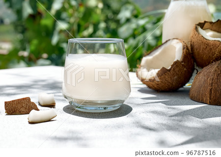 Coconut milk in glass and half of coconut on palm leaf background. Vegetable milk, lactose free non dairy healthy drink. Vegan food. 96787516