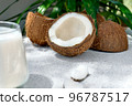 Half of coconut and coconut milk in drinking glass on palm leaf background. Vegetable milk, lactose free non dairy healthy drink. Vegan food. 96787517