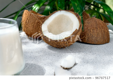 Half of coconut and coconut milk in drinking glass on palm leaf background. Vegetable milk, lactose free non dairy healthy drink. Vegan food. 96787517