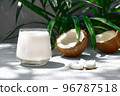 Coconut milk in glass and half of coconut on palm leaf background. Vegetable milk, lactose free non dairy healthy drink. Vegan food. 96787518